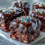 Cracked-open Chocolate Covered Rice Krispy Treats reveal crunchy cereal and gooey marshmallow layered under glossy dark chocolate.