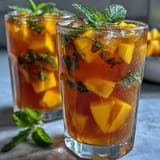 Mango peach iced tea with mint, served over ice and garnished with fresh mint sprigs and fruit slices.