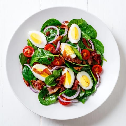 Tossed Spinach Salad with Bacon featuring halved cherry tomatoes, sliced boiled eggs, and a tangy red wine vinaigrette.