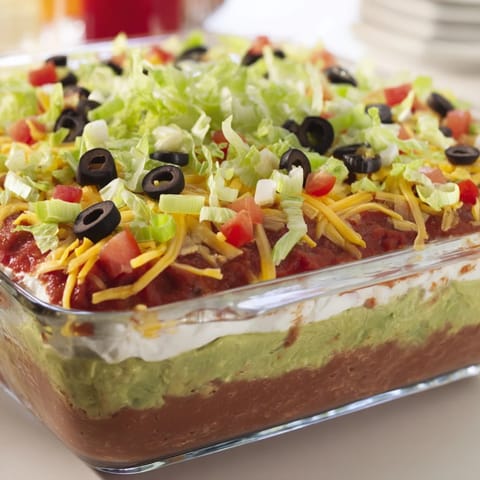 Close-up of Seven-Layer Dip showing distinct layers of guacamole, sour cream, and cheddar cheese with fresh tomato.