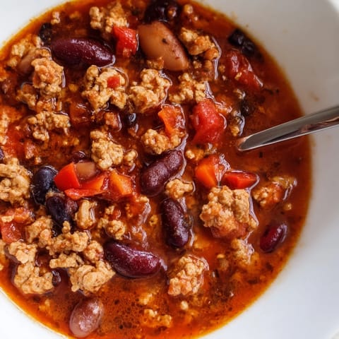 Close-up of Turkey Chili simmering in a pot, revealing a rich, thick texture with chunks of turkey, peppers, and beans.