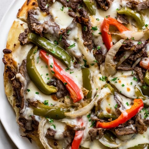Golden Philly Cheesesteak Pizza slice being lifted to show gooey cheese and tender ribeye steak inside.