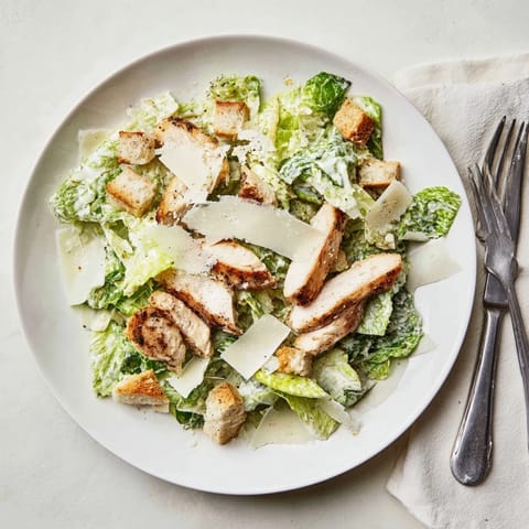 Sliced grilled chicken crowns a vibrant bowl of romaine lettuce topped with crunchy croutons and shaved Parmesan, ready to serve for dinner.