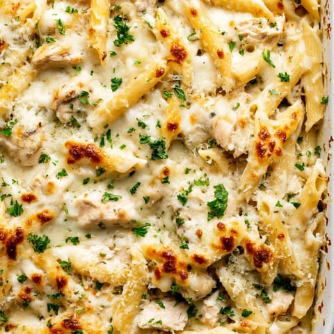 Fork lifting a cheesy bite of Chicken Alfredo Bake with creamy sauce, penne pasta, and tender chicken.