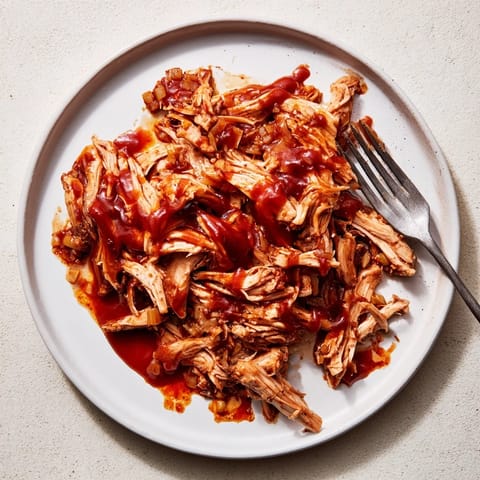 Savory BBQ Pulled Chicken served hot in a white bowl, garnished with fresh parsley alongside cornbread and baked beans.