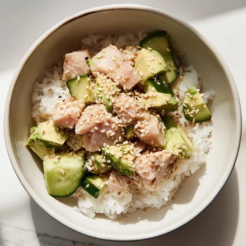 A close-up of a vibrant Tuna Avocado Rice Bowl featuring flaky tuna, diced avocado, scallions, and toasted sesame seeds on fluffy jasmine rice.