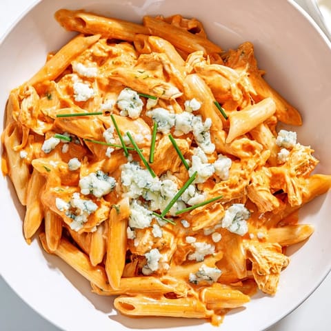 Penne noodles tossed in Buffalo Chicken Pasta, garnished with blue cheese crumbles and fresh chives on a rustic table.  