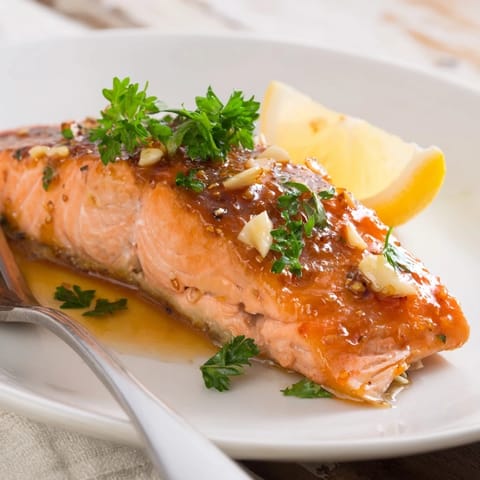 Glazed Honey Garlic Glazed Salmon fillets glisten with buttery glaze and fresh parsley garnish, served with lemon wedges on a rustic plate.