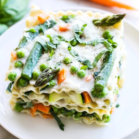 Fresh Spring Veggie Alfredo Lasagna slices on a white plate, garnished with basil and showing off colorful vegetable layers.