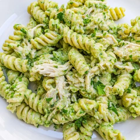 A vibrant bowl of Cilantro Lime Chicken Pasta featuring rotini and tender chicken coated in a creamy green yogurt sauce with lime wedges.