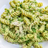 A vibrant bowl of Cilantro Lime Chicken Pasta featuring rotini and tender chicken coated in a creamy green yogurt sauce with lime wedges.