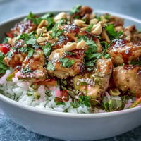Thai Peanut Chicken Bowl with fluffy coconut rice, crisp veggies, and spicy peanut sauce drizzled on top.