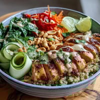 Golden-baked chicken slices rest on fluffy brown rice, surrounded by crisp cucumbers and vibrant purple cabbage in the Peanut Chicken Power Bowl.