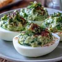 Fresh avocado deviled eggs with vibrant green filling, garnished with herbs and paprika for a healthy spring appetizer.